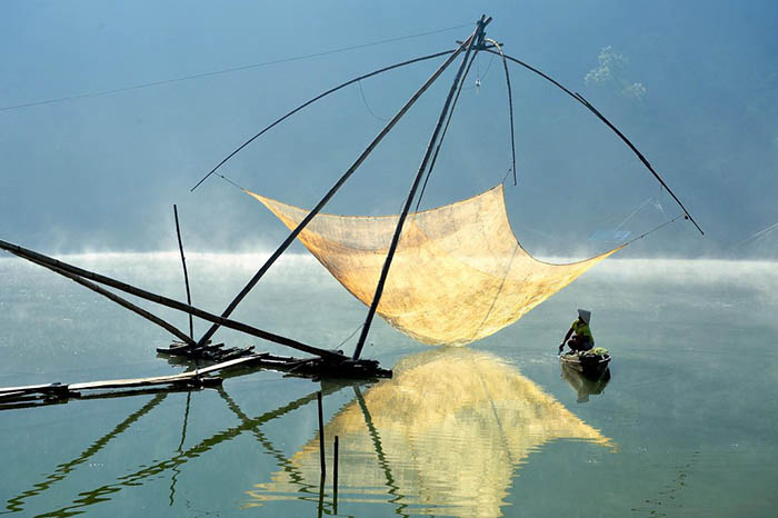 Finalist: Travel | Photograph by Hoang Long Ly – A fisherman checks his net in the early morning. At night, the fishermen of Tuyen Lam Lake lower nets into the water and turn on lights above them to lure fish. (Lam Dong, Dalat, March 2014. Nikon D700).